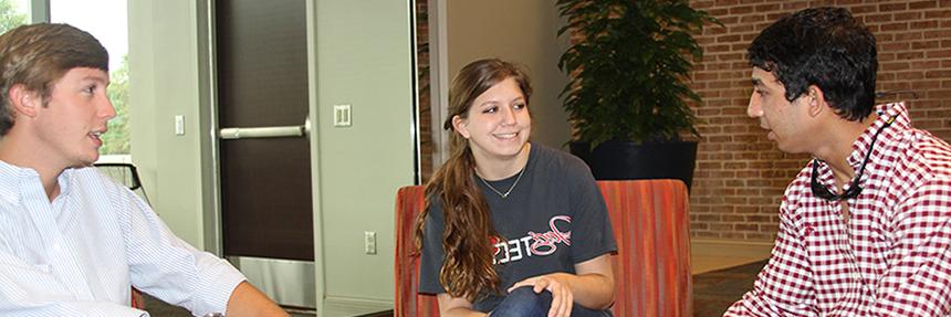 Three students sitting and talking inside of Mitchell College of Business.